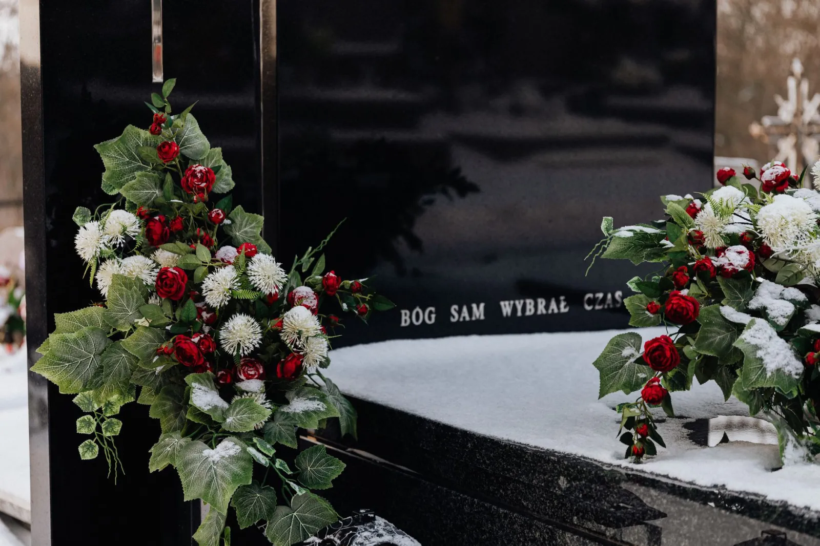 Snow-covered tombstone with red roses and white flowers, symbolizing winter's serene beauty in a cemetery.